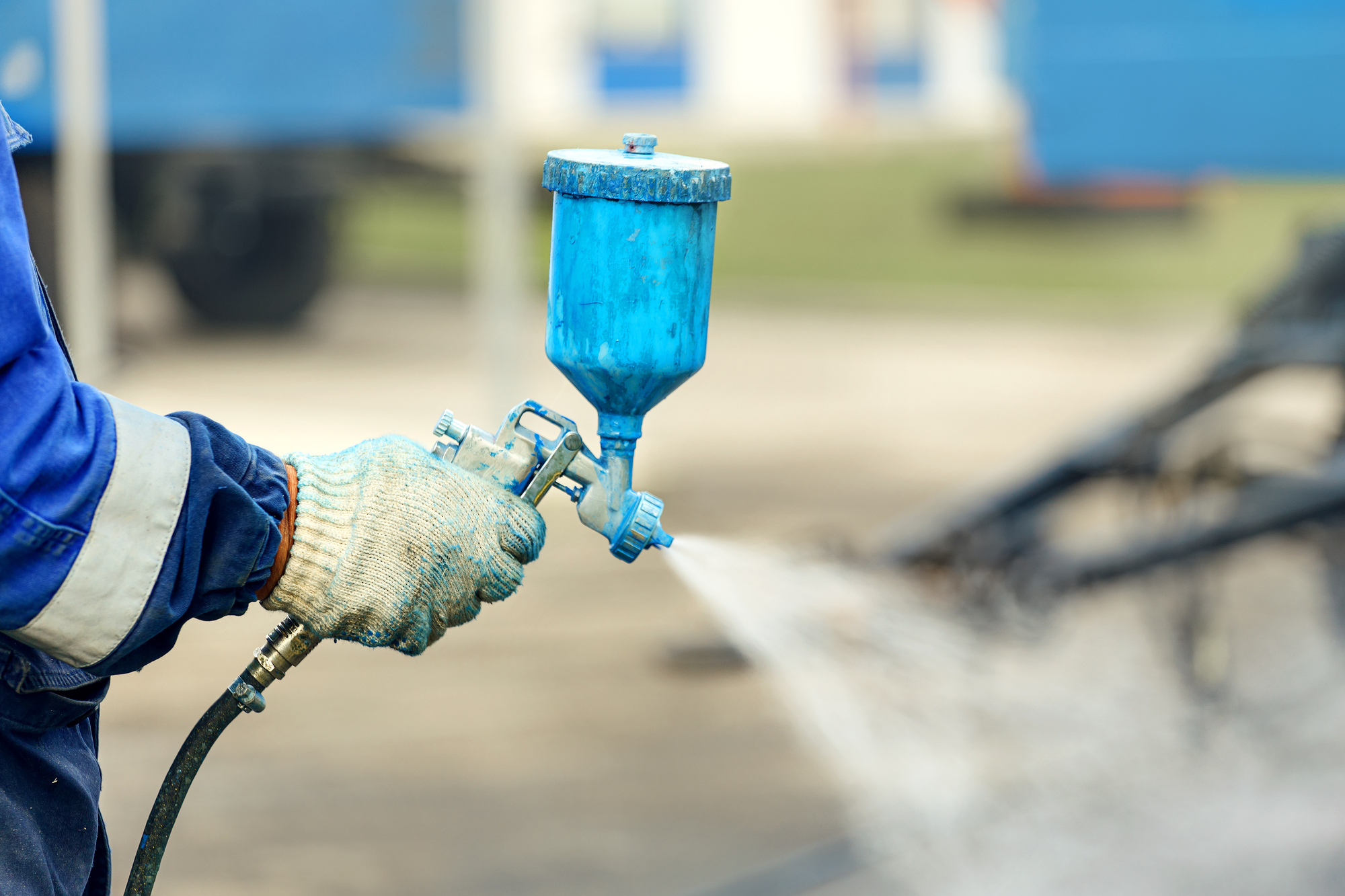 Spray gun in hand. A worker in overalls and a glove holds a spray compressor for painting in his hand.
